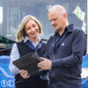 Mann und Frau stehen vor einem Bus, der Mann zeigt der Frau etwas auf dem Laptop